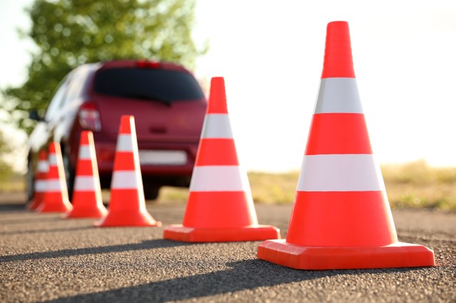 A line of traffic cones with a vehicle driving in the background away from the camera