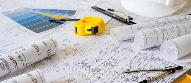 A photograph of architectural diagrams on a table, with a yellow tape measure